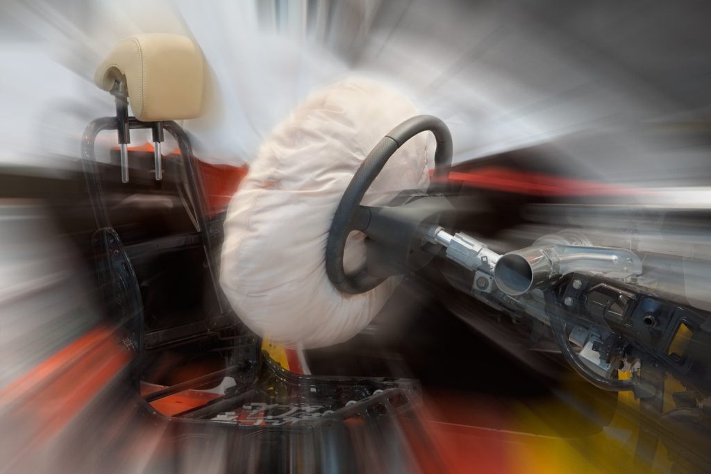 A car interior with an inflated airbag deployed from the steering wheel, shown with a motion blur effect.
