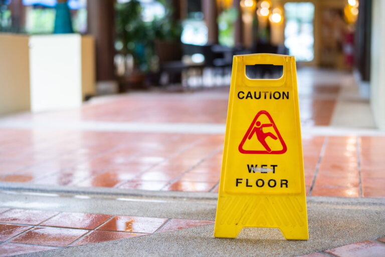 A yellow "Caution Wet Floor" sign stands on a tiled floor, warning of a slippery surface indoors.
