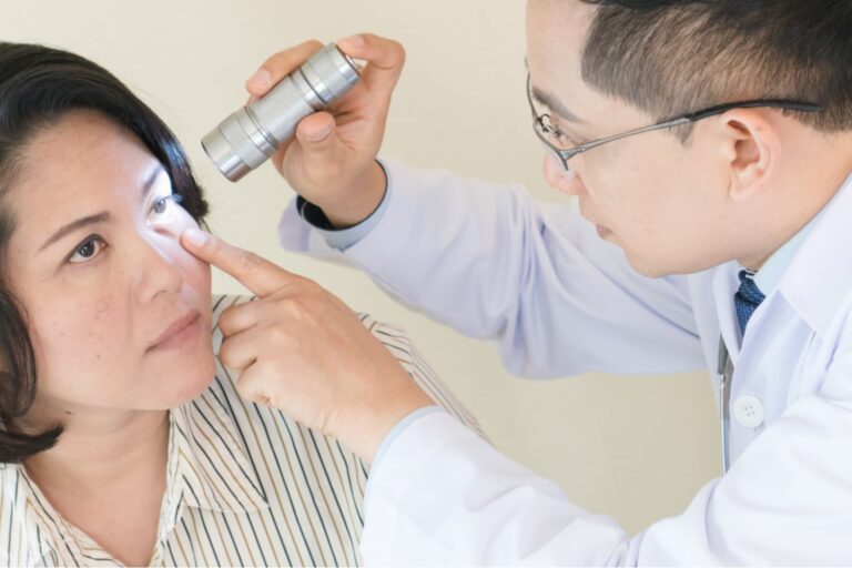 A doctor uses a handheld light to examine a patient’s eye while the patient looks upward.