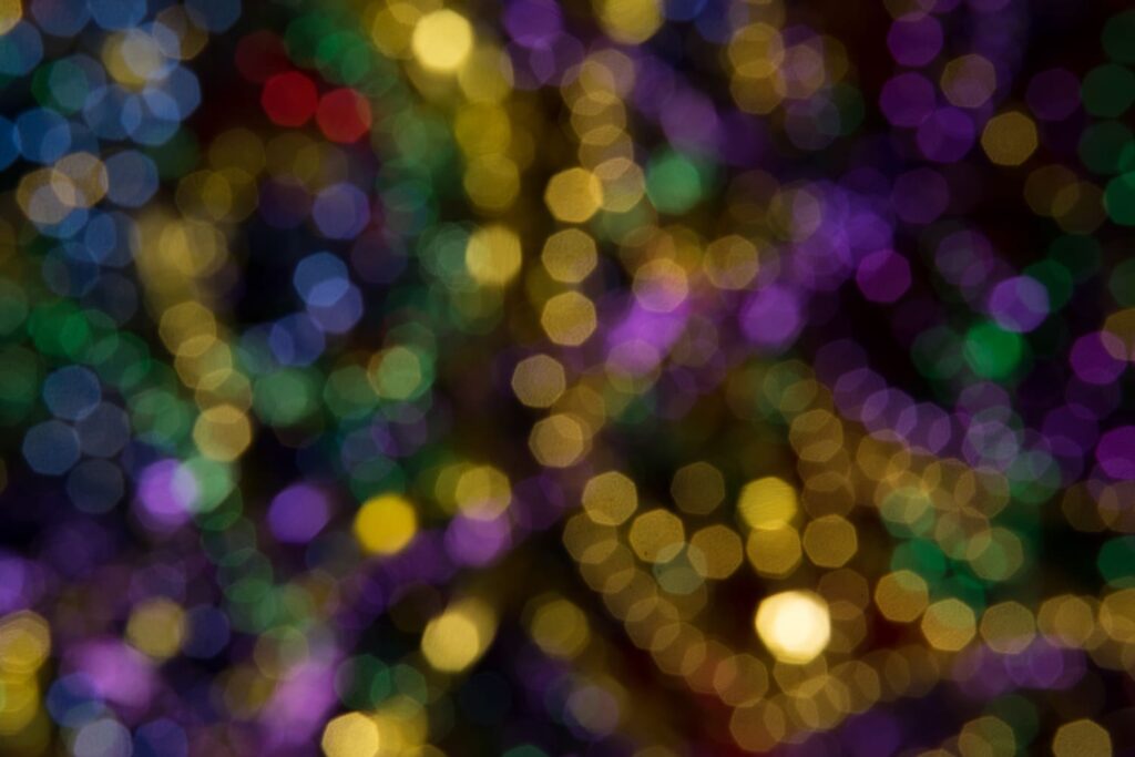 Out-of-focus image of colorful lights, including yellow, purple, blue, green, and red, creating a soft bokeh effect on a dark background.