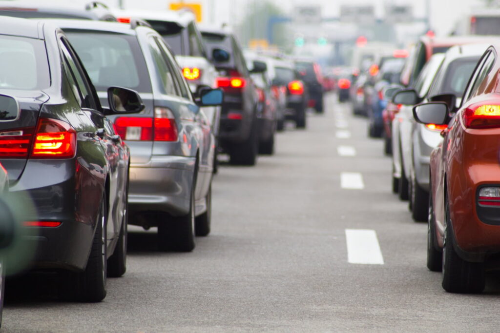 Cars are lined up bumper to bumper in heavy traffic on a multi-lane road, with brake lights illuminated.