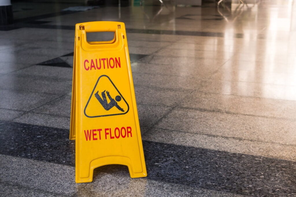 A yellow caution sign with the words "Caution Wet Floor" stands on a tiled floor, warning of a slippery surface.