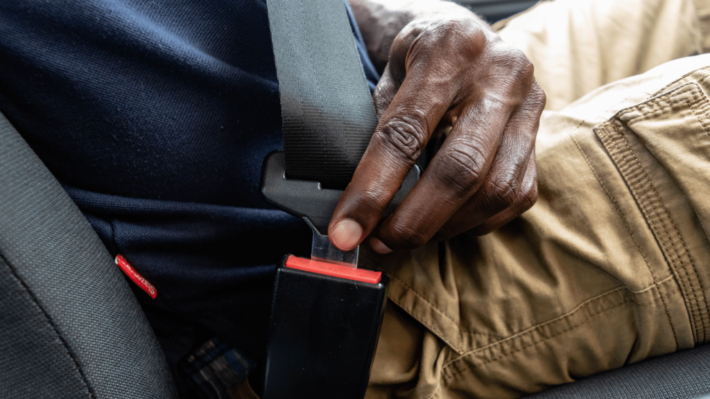 A person wearing a navy shirt and khaki pants fastens a seatbelt while sitting in a car.