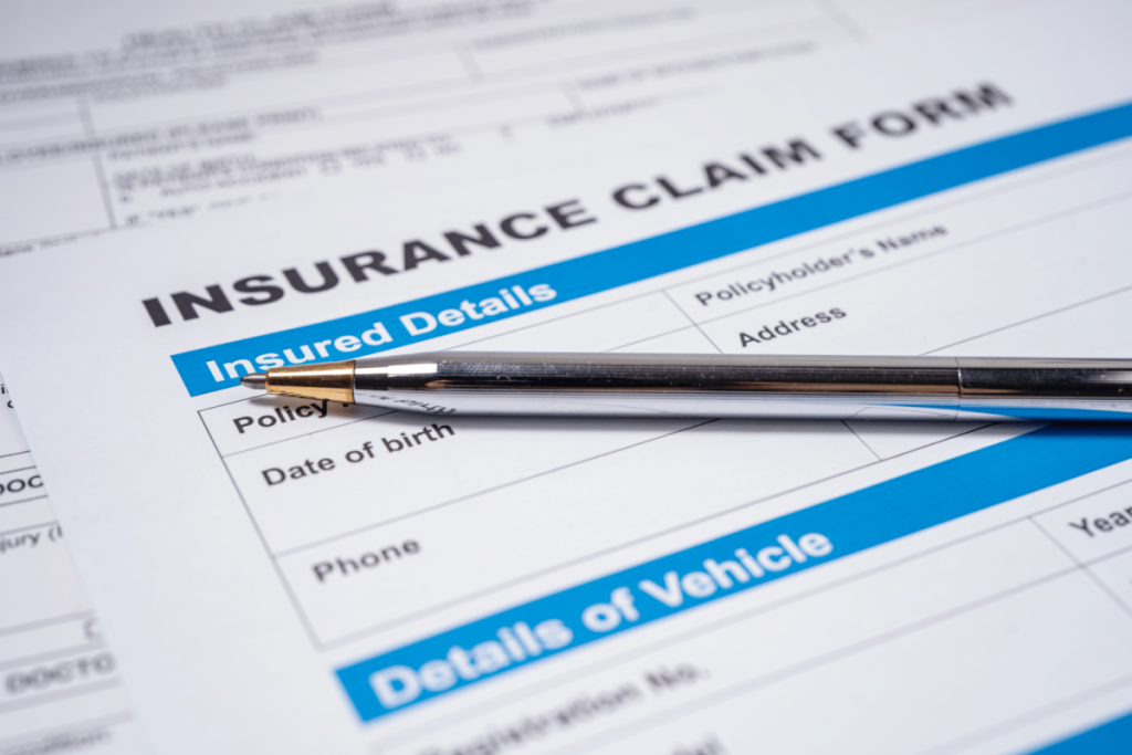 A pen resting on an insurance claim form, which includes sections for insured details and vehicle information.