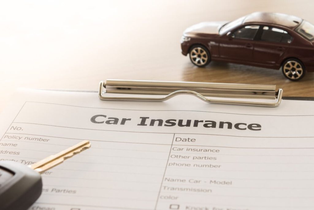 Car insurance form on a clipboard, with a car key and a model car placed on a wooden surface.