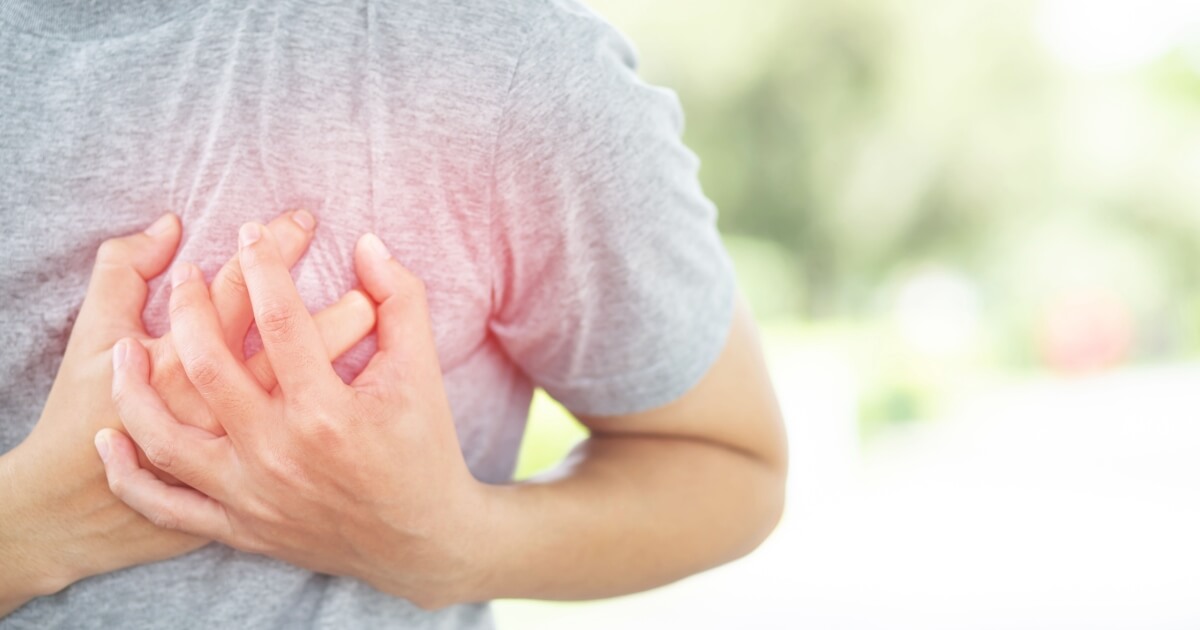 A person in a gray shirt clutching their chest with both hands, suggesting chest pain or discomfort.
