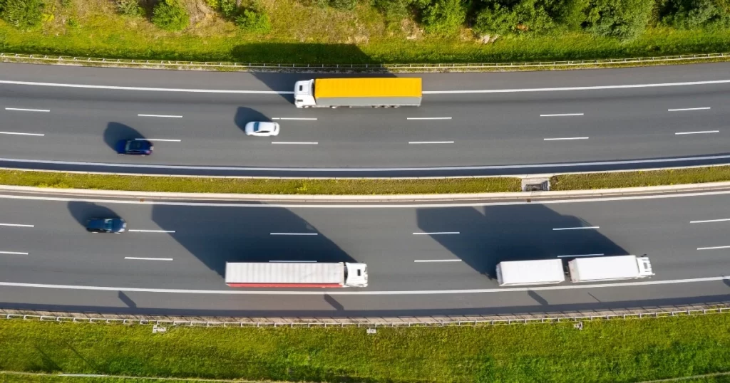 Aerial view of a divided highway with cars and trucks traveling in both directions, bordered by grass and trees.
