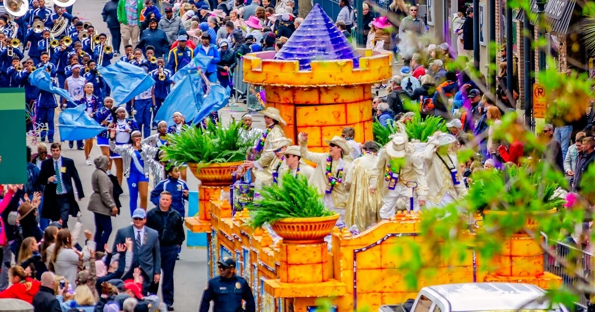 A colorful parade float shaped like a castle moves down a crowded street, surrounded by people in costumes and spectators on both sides.