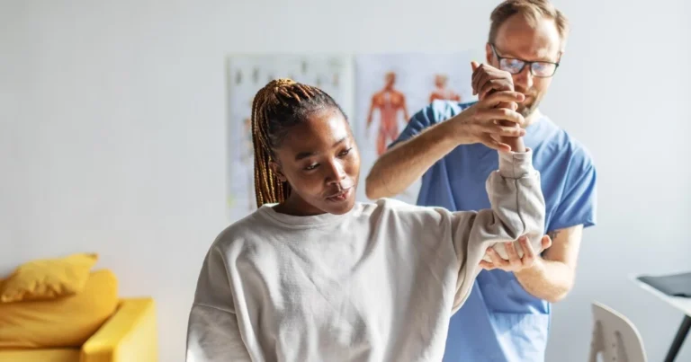 A healthcare professional assists a woman in raising her arm during a physical therapy session in a clinic.