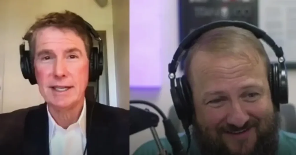 Two men wearing headphones speak into microphones during a video call interview. The man on the left wears a suit jacket, while the man on the right smiles and wears casual clothes.