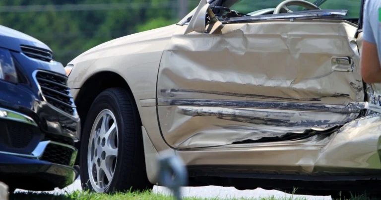 A beige car with a heavily dented driver-side door is shown after a collision with a blue vehicle.