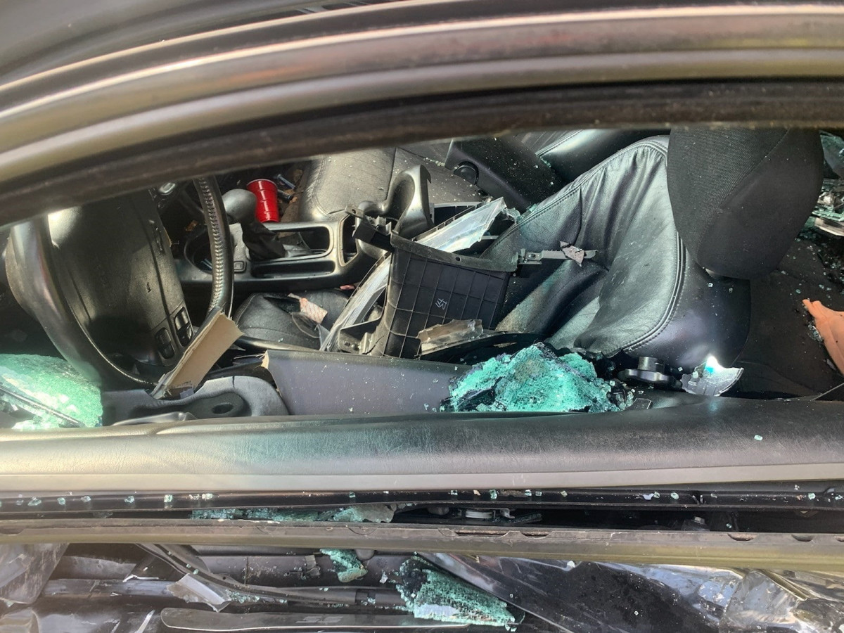 Interior of a car with a broken window, shattered glass on the seat and floor, and debris scattered inside.