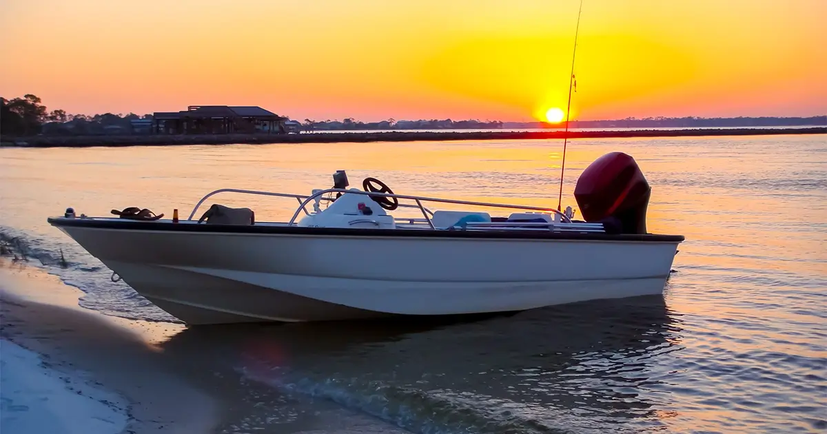 A small motorboat is beached on the shore at sunset, with calm water and a building in the background.