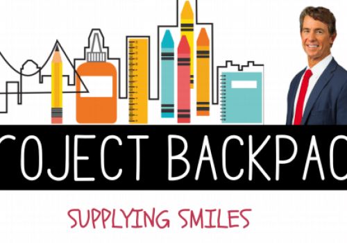 A man in a suit stands next to school supplies graphics with the text "Project Backpack" and "Supplying Smiles" written below.
