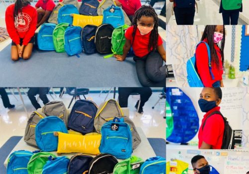 Students in a classroom and hallway, wearing red shirts and masks, pose with and carry green and blue backpacks.