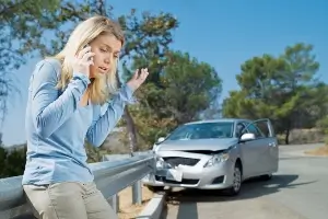 young woman on phone; crash-damaged car in background